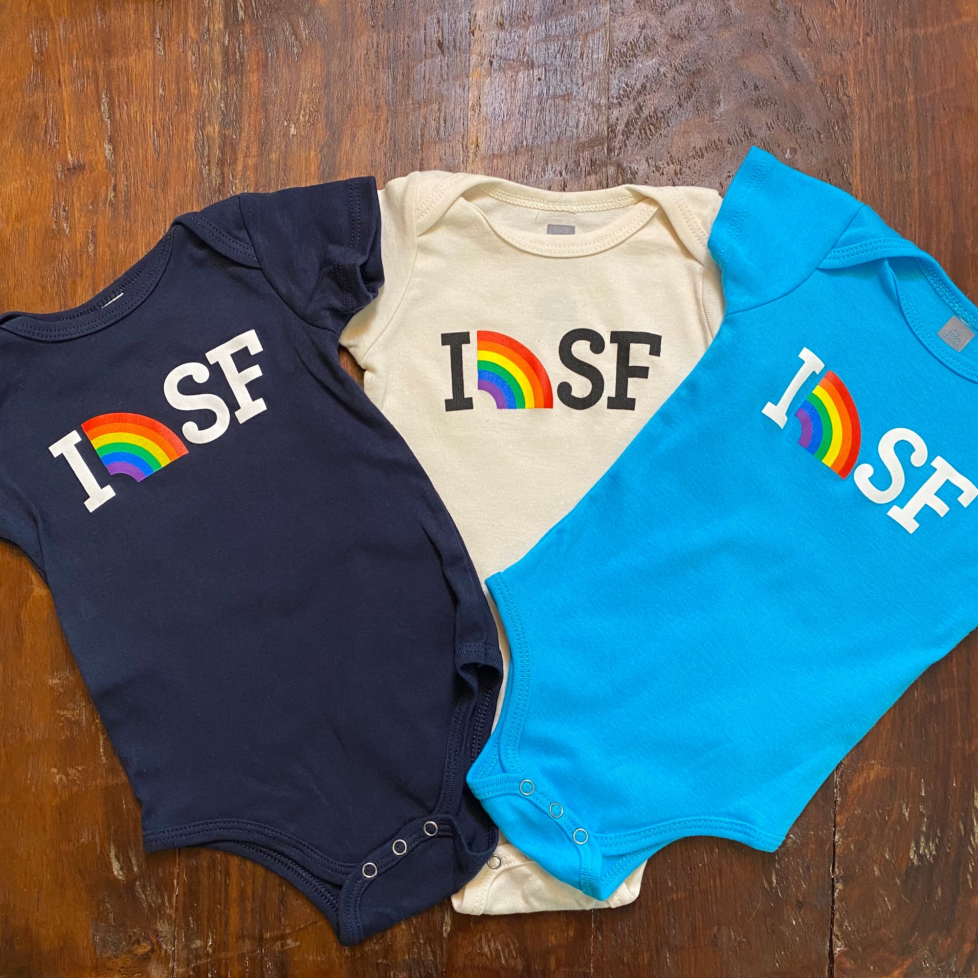 picture of dark blue, cream and aqua blue onsies with I (picture of rainbow) SF written on them