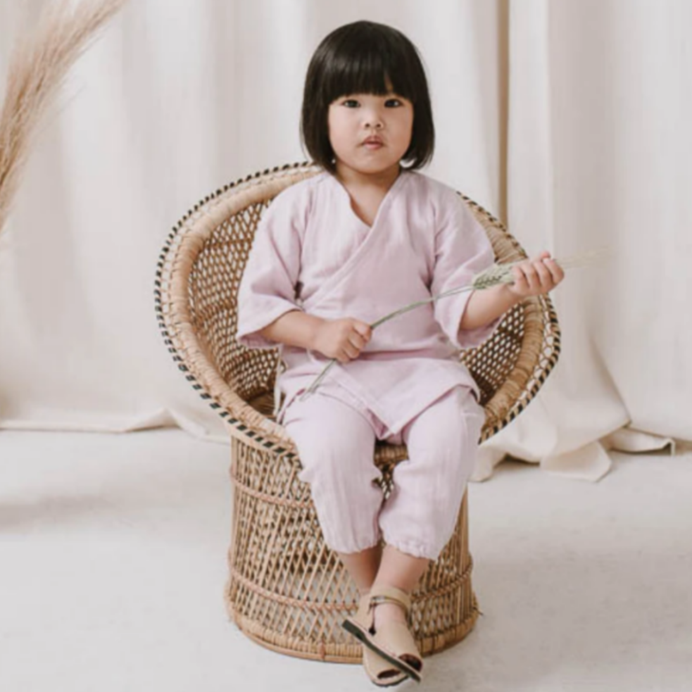 little girl wearing pink kimono top and pants sitting in rattan chair