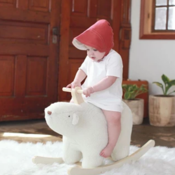 baby riding polar bear toy wearing red sun bonnet