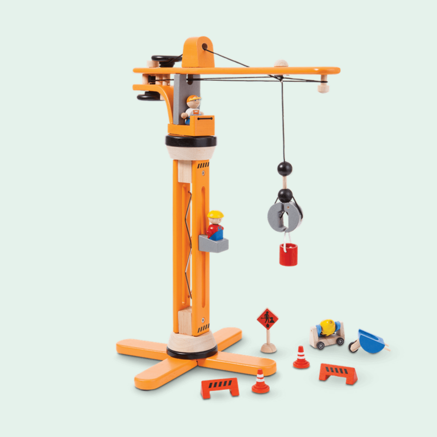 A wooden crane toy with a construction sign, street hazard sign, concrete mixer, and two figures of a foreman and worker. The crane is primarily orange with a black pulley and metallic accents.