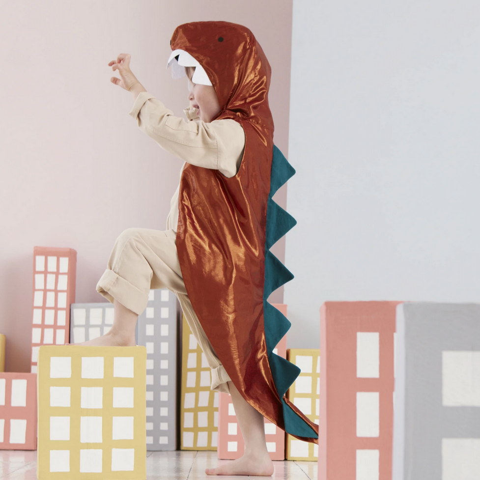 kid wearing brown dinosaur costum with blue spikes and fake buildings