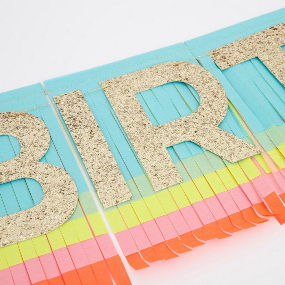 detail of rainbow colored fringe garland with gold glittered Happy birthday letters on top