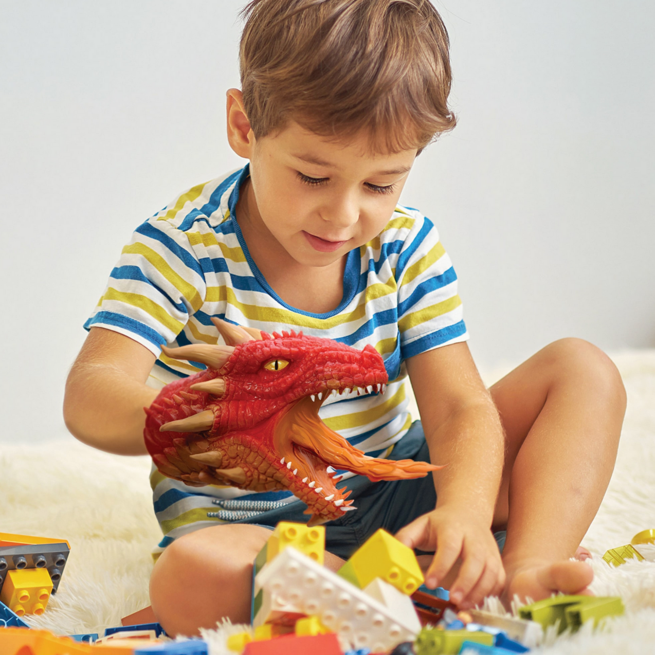 boy wearing red dragon hand puppet over legos