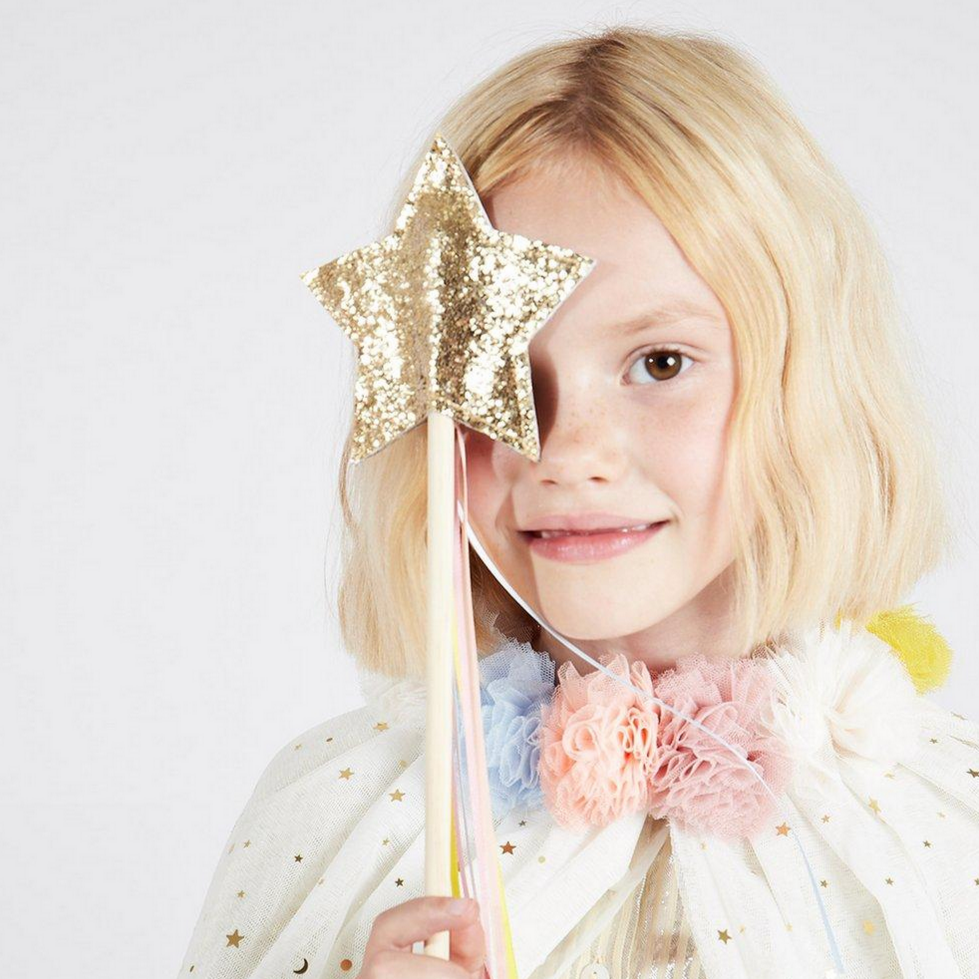 little girl with pompom tulle color holding glittered star wand up to eye. wand has colored ribbons hanging down.