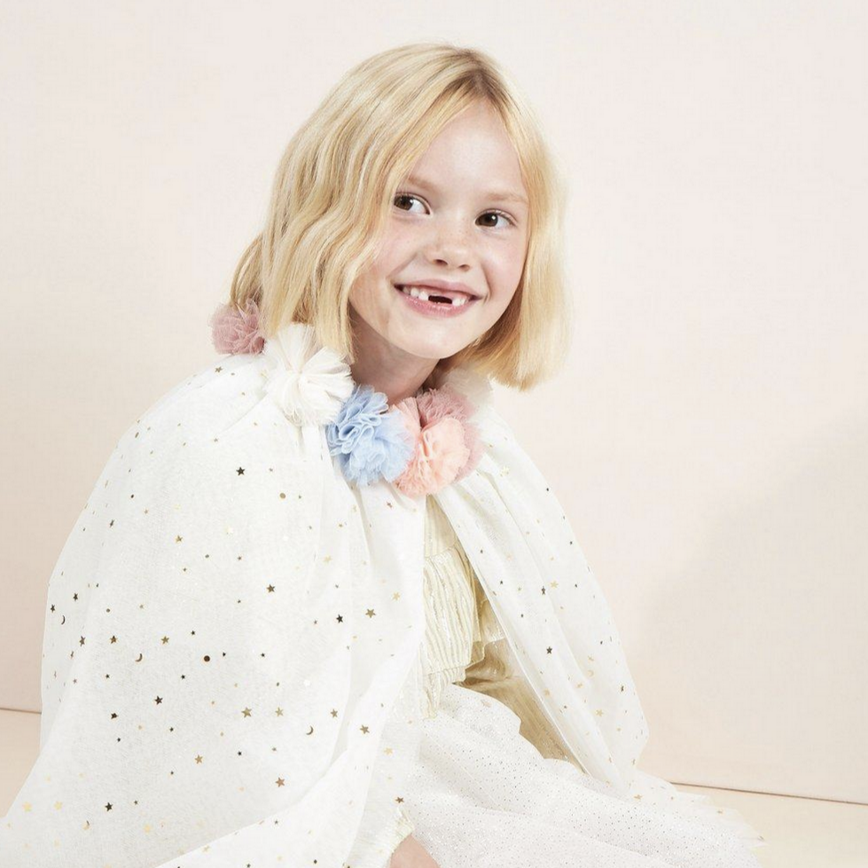 little girl smiling wearing sparkly cape with pompom collar