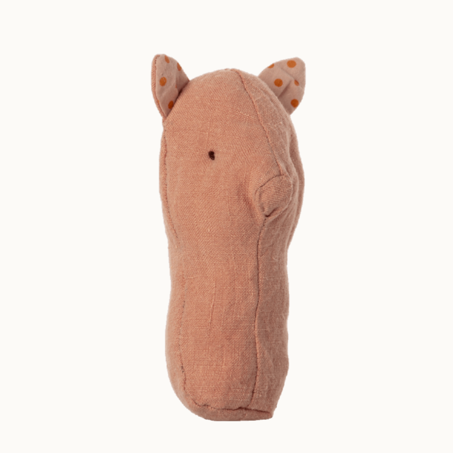 A beige-colored fabric rattle in the shape of a pig with a small dot pattern for eyes and a stitched line for a nose.