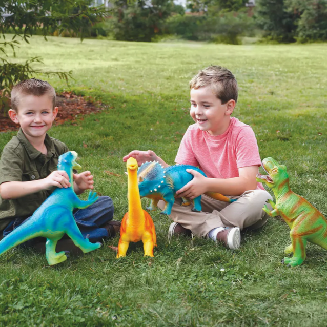 Two children sitting on grass playing with colorful rubber dinosaur toys.