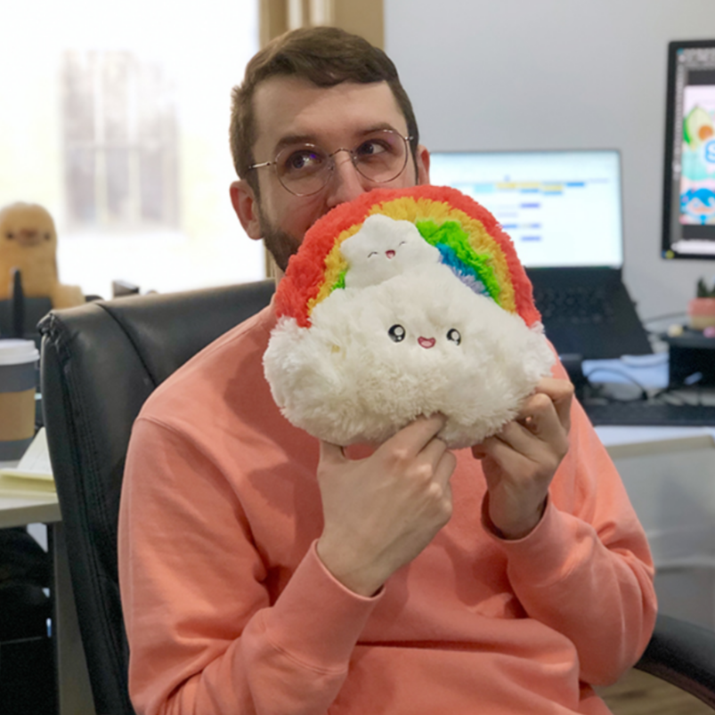 man woth glasses holding rainbow plush