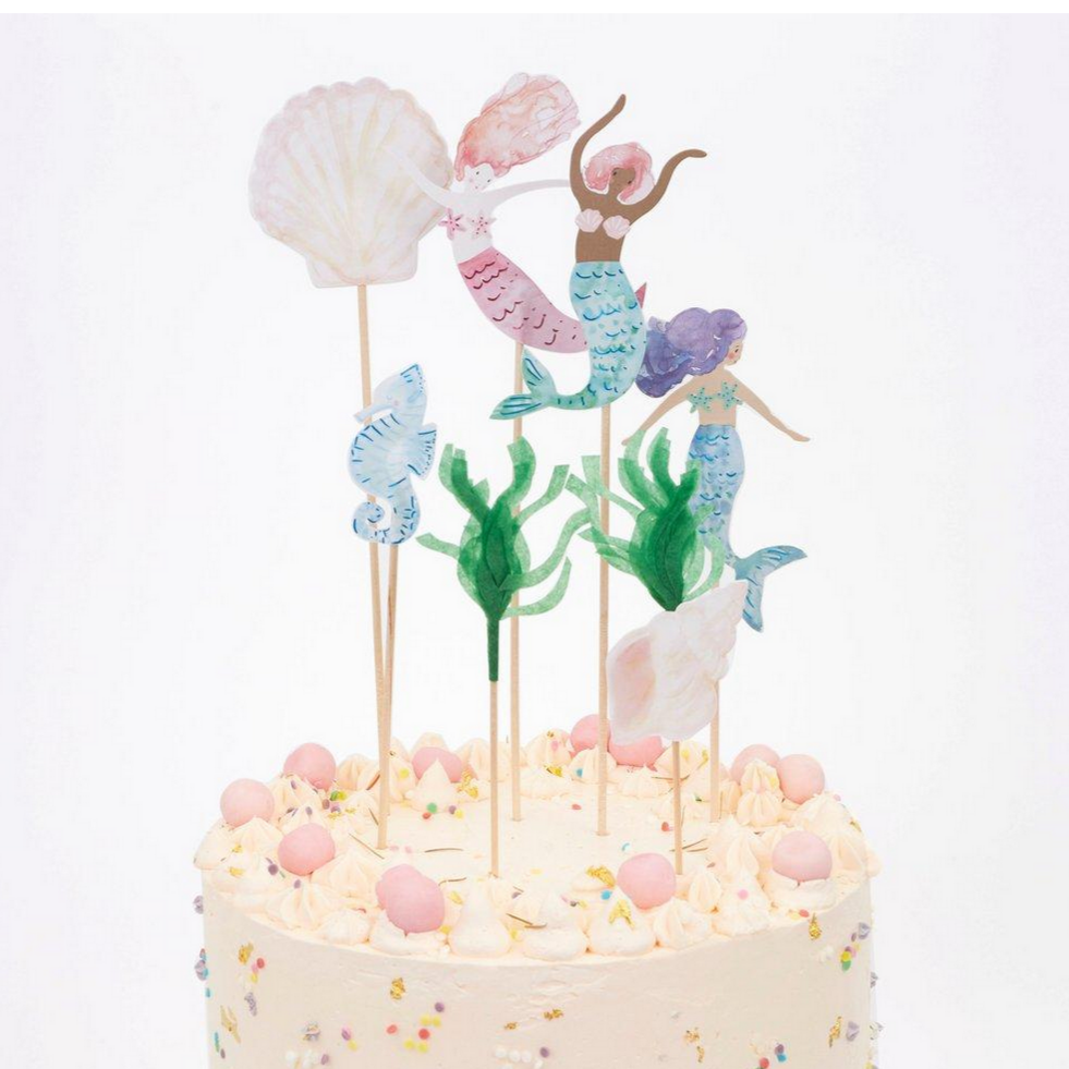 3 mermaids, two shells, a seahorse and tissue grass on long wooden sticks on top of a cake