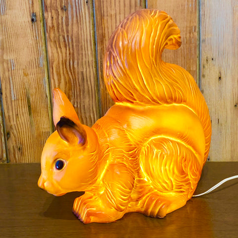 picture is of the squirrel lamp lit and sitting on a brown shelf